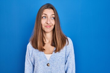 Young woman standing over blue background smiling looking to the side and staring away thinking.