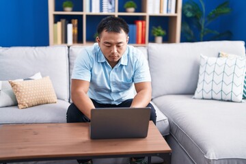 Young chinese man using laptop with serious expression at home