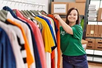 Naklejka na ściany i meble Brunette woman with down syndrome looking at donated clothes at donations stand