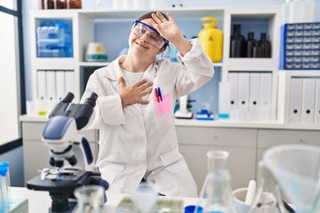 Hispanic girl with down syndrome working at scientist laboratory touching forehead for illness and fever, flu and cold, virus sick