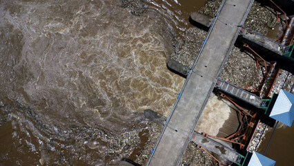 Aerial view of the water released from the concrete dam's drainage channel as the overflow in the rainy season. Top view of turbid brown forest water flows from a dam in rural northern Thailand.