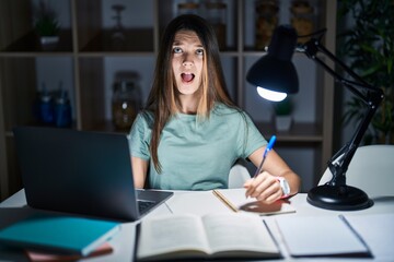 Teenager girl doing homework at home late at night angry and mad screaming frustrated and furious, shouting with anger. rage and aggressive concept.