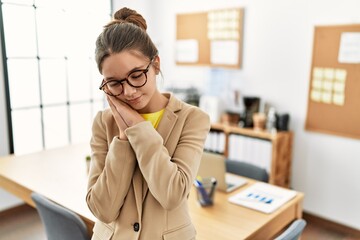Young brunette teenager wearing business style at office sleeping tired dreaming and posing with...
