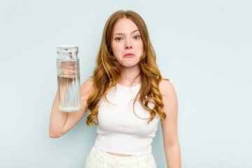 Young caucasian woman holding jar of water isolated on blue background shrugs shoulders and open eyes confused.