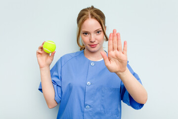 Young caucasian physiotherapist holding a tennis ball isolated on blue background standing with...