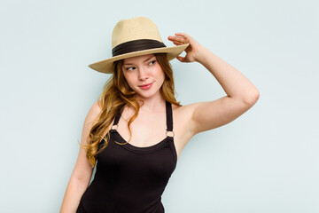 Young caucasian woman going to the beach isolated on blue background touching back of head, thinking and making a choice.