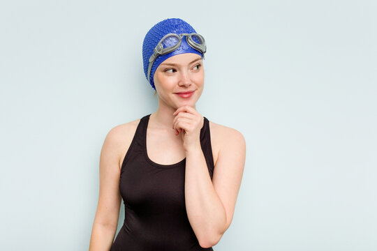 Young caucasian swimmer woman isolated on blue background looking sideways with doubtful and skeptical expression.