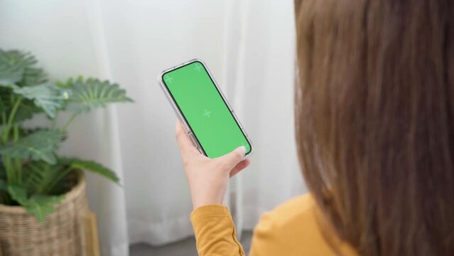 Woman using green screen for copy space closeup. Mock-up on smartphone in hand, female sitting on bed holding mobile phone and touch screen while looking social network at home.
