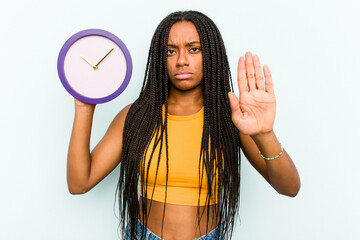 Young African American woman holding a clock isolated on blue background standing with outstretched...