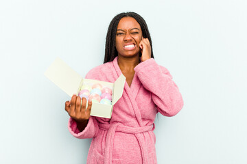 Young African American woman holding an aromatic balls for bathtub isolated on blue background covering ears with hands.