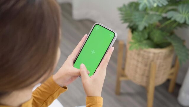 Woman using green screen for copy space closeup. Chroma key mock-up on smartphone in hand, female sitting on bed holding mobile phone and touch screen while looking social.
