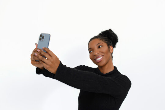Happy African American woman with phone. Female model in turtleneck with curly hair taking selfie in studio. Portrait, studio shot, emotion concept