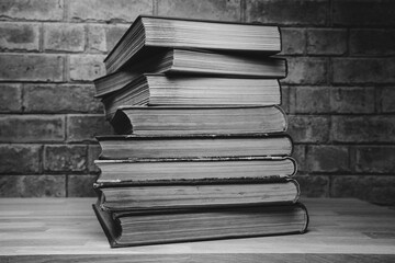 Books lying on top of each other on a wooden table against the background of a brick wall.