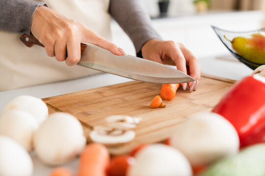 Cropped closeup image of woman chef housewife cutting vegetables mushrooms at home kitchen, preparing salad soup, cooking vegan healthy vegetarian meal