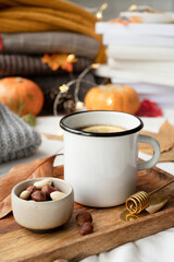Cozy autumn composition, sweater weather. Hot tea with lemon and nuts on wooden tray surrounded with autumn leaves and sweaters, mug mockup design