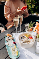 Beautiful Woman eating fresh oysters and drinking chilled prosecco wine on the summer sunset in restaurant. Seafood delicacies