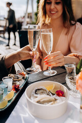 Two Women friends eating fresh oysters and drinking chilled prosecco wine on the summer sunset in restaurant. Seafood delicacies