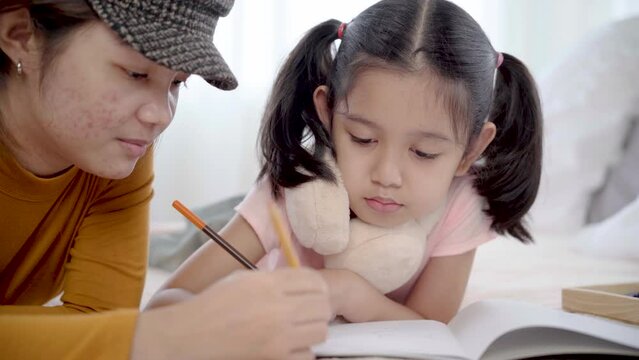 Sibling drawing in paper together on bed, elder sister and adorable little girl enjoying hobby pastime alone without parents in bedroom. Nanny teaching children draw in holiday, using colorful pencils