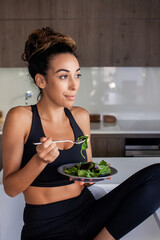 Attractive woman eating salad in morning. Woman in sportive clothes getting ready for new day. Home, morning routine, food concept