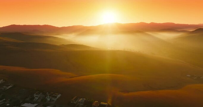 Beautiful hills in the bright rays of sun hiding behind the mountain. Drone flight over the city locating in the mountainous territory. Aerial view.
