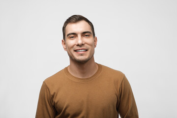 male portrait, 30-year-old smiling caucasian man in brown beige sweatshirt on gray background