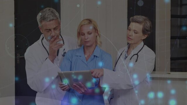 Animation of blue glowing spots over team of medical health workers using digital tablet at hospital