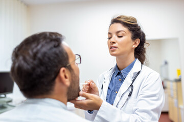 Male patient opening his mouth for the doctor to look at his throat. Female doctor examining sore throat of patient in clinic. Otolaryngologist examines sore throat of patient.