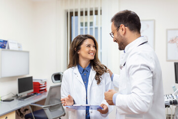 Obraz premium Doctors discussing over a medical report in hospital. Female and male doctor checking clinical report of patient online. Healthcare staff having discussion in a office of private clinic.