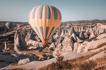 Naklejka premium Colorful hot air balloon preparing to rise up for sunset watching tour over spectacular Cappadocia mountains. Wide landscape of Goreme valley. Vintage retro orange blue toning filter. Tourism, travel