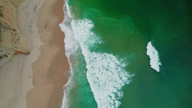 Aerial view drone shot pan up of rock cliffs on California Coastline.  View of waves crashing on the beach