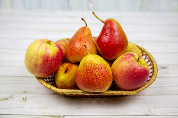 Bright pink apples and pears in a wicker basket on a table made of gray boards. Vegetables and fruits. Useful products.