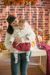 A young mother and little daughter in white warm knitted sweaters in an interior decorated with blankets and pillows
 as well as pumpkins, autumn leaves and apples. Autumn mood. halloween