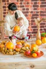 A young mother and little daughter in white warm knitted sweaters in an interior decorated with blankets and pillows
 as well as pumpkins, autumn leaves and apples. Autumn mood. halloween
