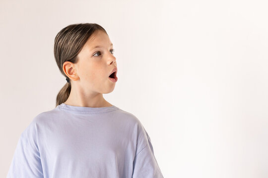 Portrait of astonished preteen girl wearing blue T-shirt looking away. Surprised Caucasian child posing against white background. Surprise concept