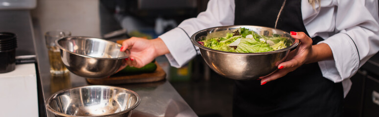 cropped view of african american chef holding bowl with salad in professional kitchen, banner.
