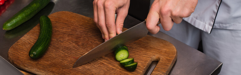 cropped view of chef cutting cucumber on wooden cutting board, banner.