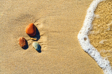 Varicolored stones on the sand with a wave and with foam. Top view, closeup. Background.