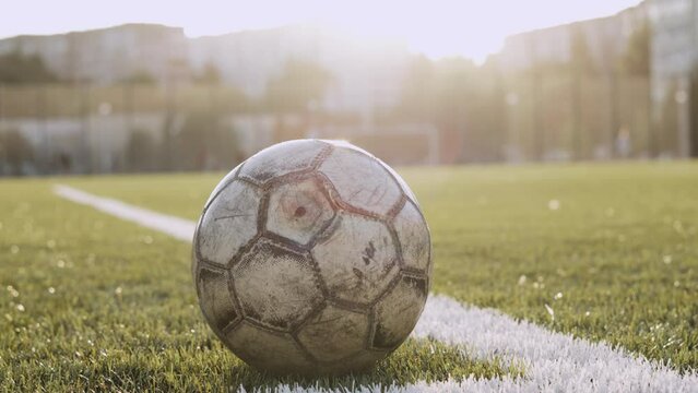 Old soccer ball lies on grass of football pitch near white lines.