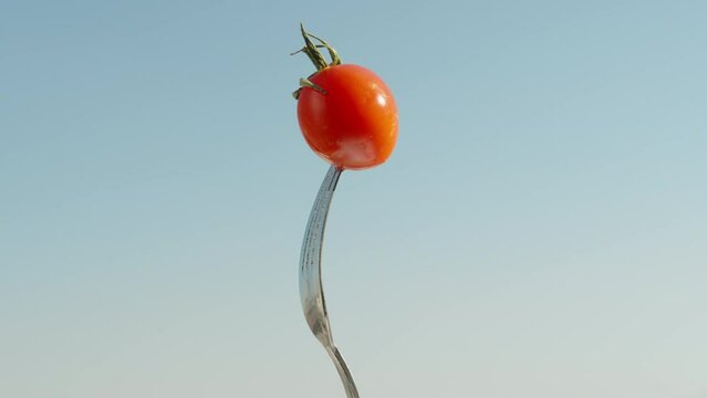 A small tomato, impaled on a fork, rotates against the blue sky. close-up
