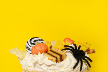 Halloween cake or dessert decorated by pumpkins and spider, yellow background with copy space