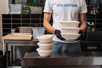 cropped view of man in t-shirt with volunteer lettering holding plastic containers in kitchen.
