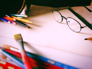 机に置かれたメガネとスケッチブックと絵筆と色鉛筆