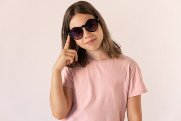 Fototapeta premium Portrait of preteen girl wearing pink T-shirt and sunglasses. Stylish Caucasian child posing against white background. Fashion concept