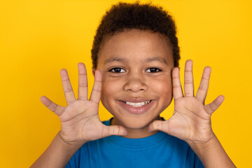 Close-up of funny preteen boy wearing blue T-shirt making face. Happy mixed race child showing palms against yellow background. Fun concept