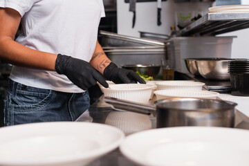 partial view of tattooed african american woman holding plastic bowl with soup in kitchen.