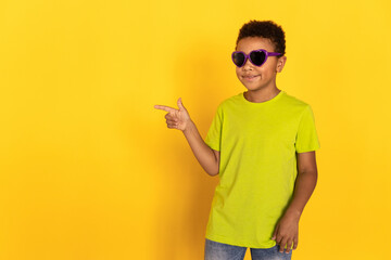 Portrait of happy preteen boy in sunglasses showing something. Mixed race child wearing green...