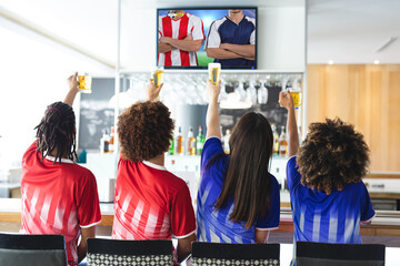 Diverse friends in bar watching tv with football match on screen