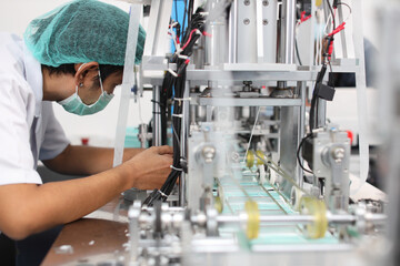 Asian worker inspecting quality of mask and medical face mask production line, Industry and factory concept.