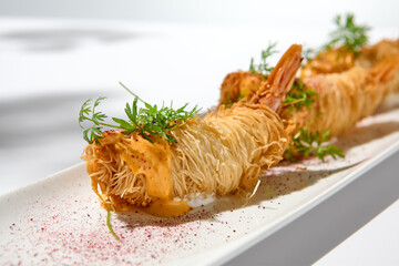 Traditional greek appetizer - kataifi wrapped shrimps on white plate. Crispy shrimp in kataifi crust in summer day. Shrimp appetizer fried in kataifi dough. Crispy prawns in modern style.
