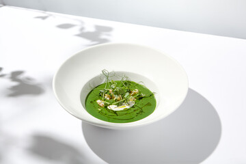 Healthy green cream soup with fish and pea. Spinach soup puree on white plate with shadows. Summer menu - broccoli cream with fish. Cream soup of green pea in vegan menu.